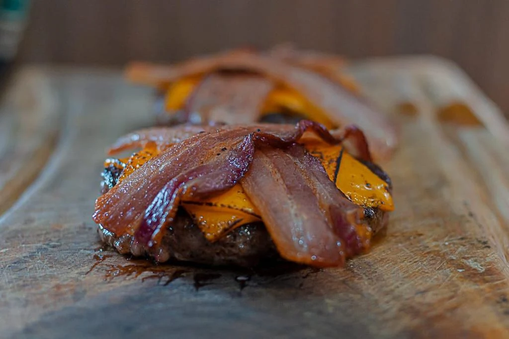 Hambúrguer dourado com queijo e bacon sobre tábua